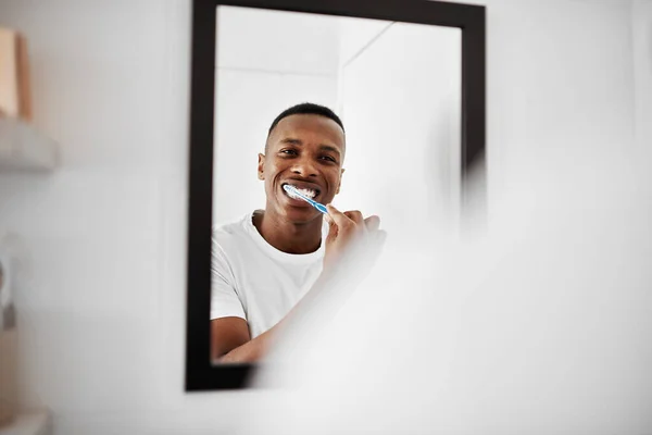 Tutti vogliono denti sani. Girato di un giovane uomo che si lava i denti mentre guarda nello specchio del bagno. — Foto Stock