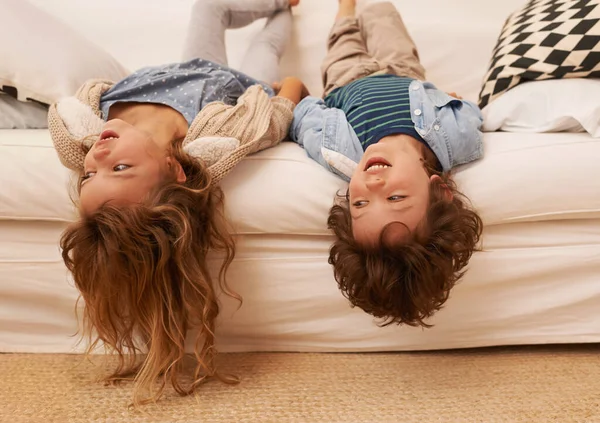 Hanging around with nothing to do. Shot of two young children lying on a sofa with their heads hanging over the edge. — Stock Photo, Image