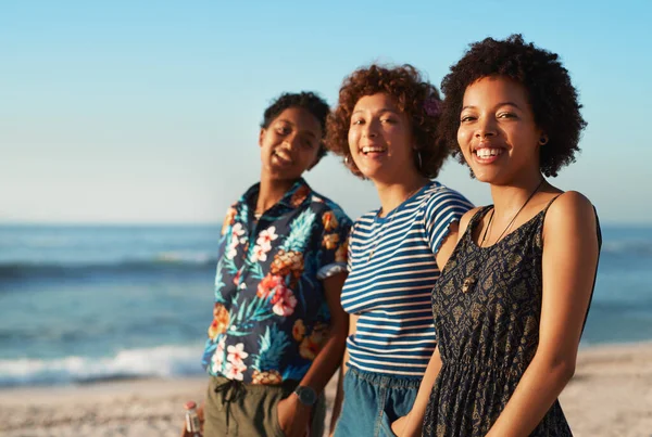 Vi får hverandre til å smile. Portrett av tre attraktive unge kvinner som står sammen og poserer på stranda om dagen. – stockfoto