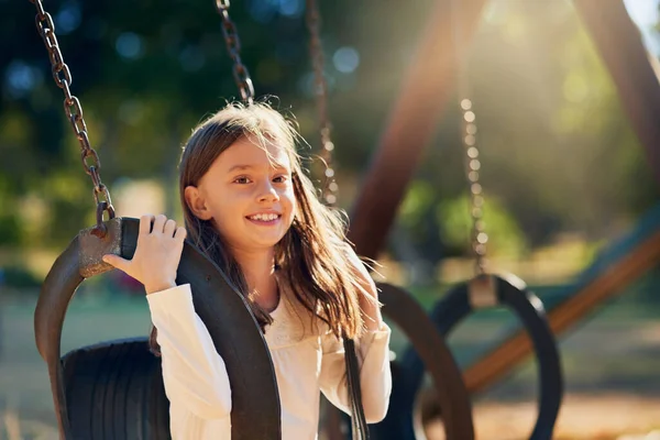 Een geweldige dag tegemoet gaan. Shot van een gelukkig klein meisje hebben plezier op de schommels in de speeltuin. — Stockfoto