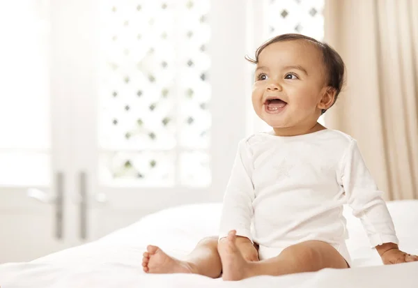 She has the cutest smile. Shot of an adorable baby girl sitting on a bed. — Stock Photo, Image