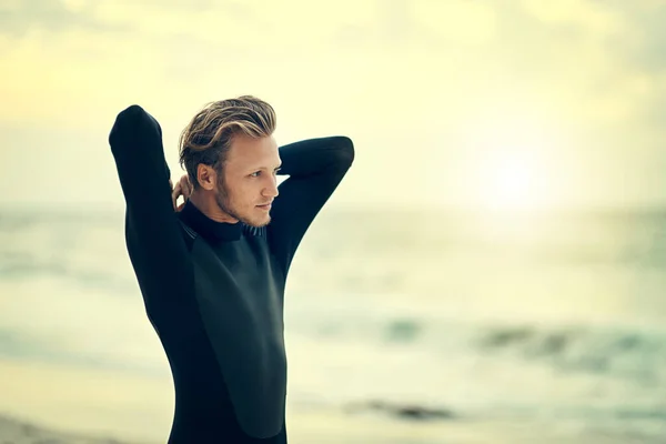 Húzd fel a cipzárt és menj ki. Vágott kép egy fiatalemberről, aki a szörfdeszkáját cipeli a parton.. — Stock Fotó
