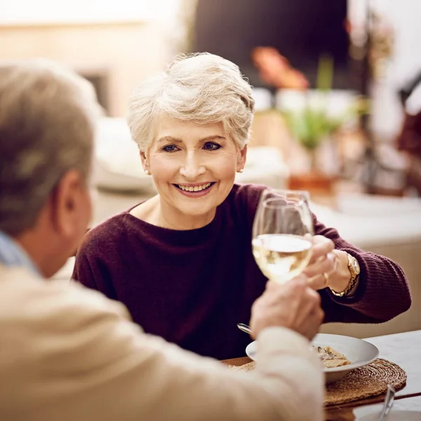 Proost, mijn liefste. Shot van een ouder stel toosten met wijnglazen terwijl ze genieten van een maaltijd thuis. — Stockfoto