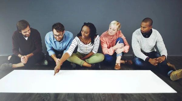 Groot papier voor een groot plan. Studio shot van een groep mensen die op de vloer zitten en werken aan blanco papier tegen een grijze achtergrond. — Stockfoto