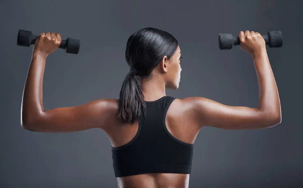 Het lichaam dat je wilt wordt verdiend door vastberadenheid. Studio shot van een sportieve jonge vrouw tillen gewichten tegen een grijze achtergrond. — Stockfoto
