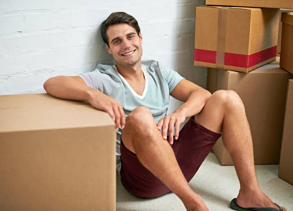 Кто-нибудь хочет помочь мне распаковать вещи. Портрет молодого человека, сидящего в своем новом доме в окружении картонных коробок. — стоковое фото