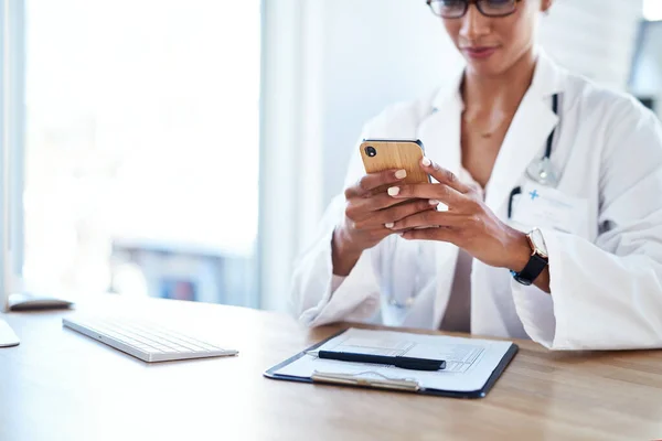 똑똑 한 의사를 위한 똑똑 한 앱이죠. 상담 실에서 스마트폰을 사용하는 젊은 의사를 찍은 사진. — 스톡 사진
