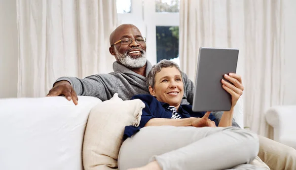 Pasar el día juntos en casa. Foto de una pareja mayor cariñosa usando una tableta mientras se relaja en el sofá en casa. —  Fotos de Stock