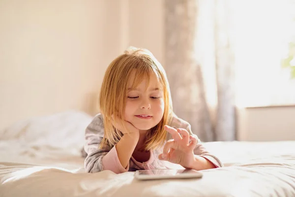 Divertimento online, quando vuoi. Girato di una bambina che gioca con il suo tablet mentre è sdraiata sul letto a casa. — Foto Stock