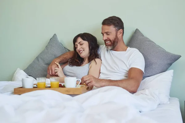 З чого нам слід почати. Знімок веселої молодої пари, сидячи в ліжку, насолоджуючись сніданком разом в ранкові години . — стокове фото