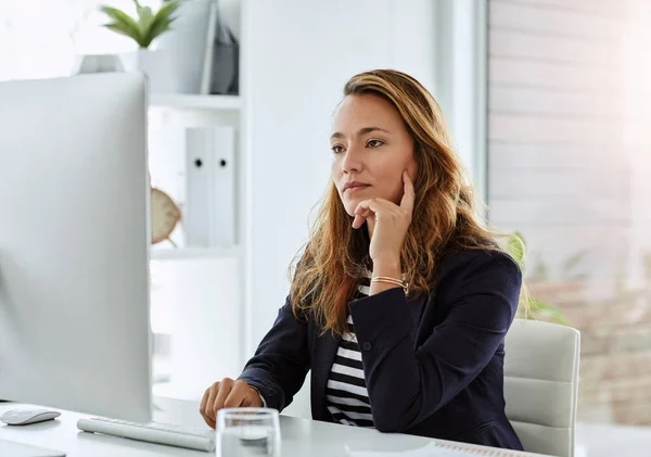 Elle réfléchit attentivement à la question. Prise de vue d'une femme d'affaires attrayante regardant réfléchi tout en travaillant sur un ordinateur dans son bureau. — Photo