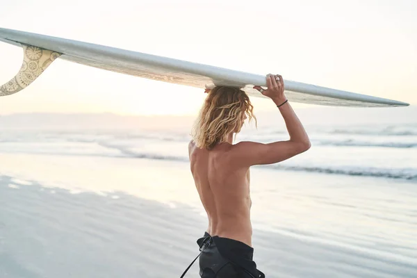 Rakt in i det djupblå havet går vi. Rearview skott av en ung surfare som bär sin surfbräda över huvudet på stranden. — Stockfoto