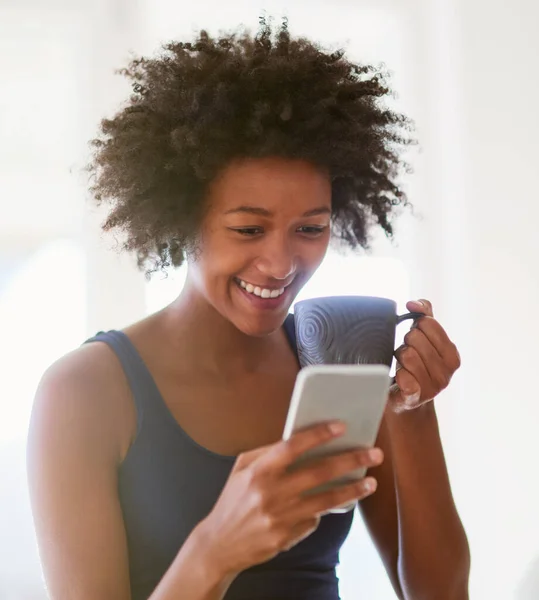 Conversas sobre café. Tiro de uma jovem atraente bebendo café em casa enquanto lê uma mensagem de texto. — Fotografia de Stock