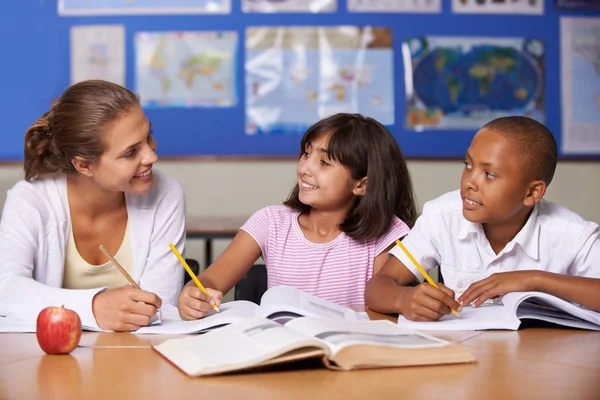 Eine positive Verstärkung. Eine junge Lehrerin diskutiert mit ihren beiden ethnischen Schülern, während sie in einem Lehrbuch blättern. — Stockfoto