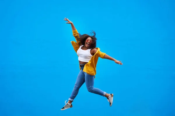 Én vagyok a világ ura. Teljes hosszúságú felvétel egy boldog fiatal nőről, aki kék háttérrel ugrik a levegőbe.. — Stock Fotó