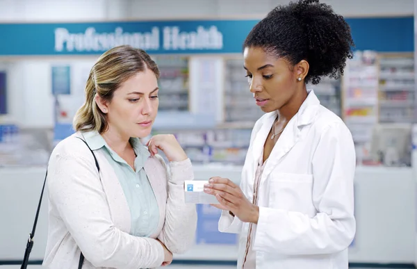 Spieghiamo sempre in dettaglio per aiutarvi a scegliere più intelligente. Foto di un giovane farmacista che raccomanda un prodotto sanitario a una giovane donna in una farmacia. — Foto Stock