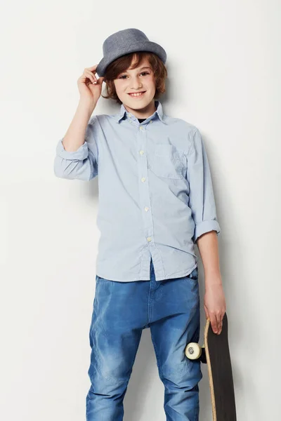 É um jovem encantador. Bonito menino pré-adolescente vestindo trajes da moda e segurando um skate enquanto isolado no branco. — Fotografia de Stock
