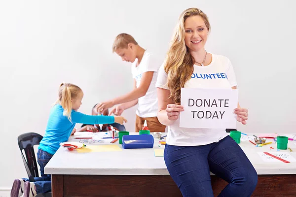 Twoja pomoc jest zawsze potrzebna. Portret wolontariuszki trzymającej dziś znak dawcy podczas pracy z małymi dziećmi. — Zdjęcie stockowe