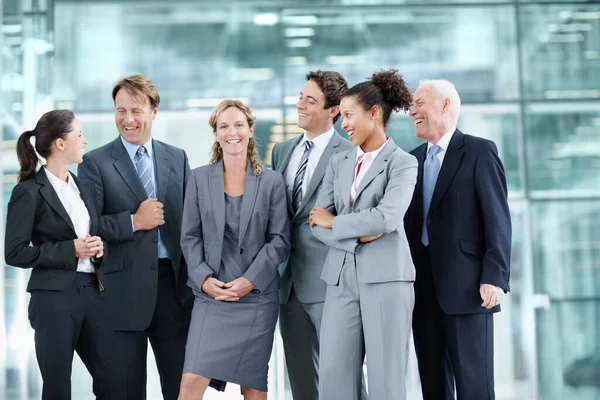 Apoiada pela sua orgulhosa equipa de colegas de trabalho. Grupo positivo de empresários que estão juntos e sorrindo enquanto cercam um colega de trabalho - retrato. — Fotografia de Stock