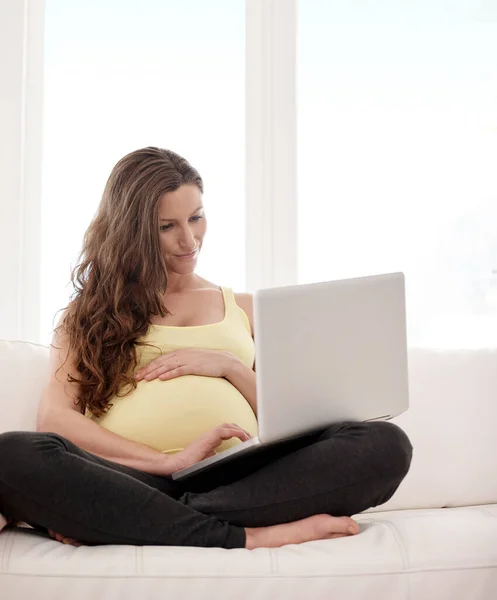 गर्भधारणेच्या टिप्ससाठी ब्राउझिंग. घरी तिच्या लॅपटॉपवर काम करणार्या तरुण गर्भवती महिलेचा शॉट . — स्टॉक फोटो, इमेज