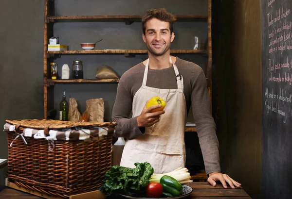 Hadd készítsek valami finomat és egészségeset. Egy fiatal férfi portréja, aki a konyhában áll friss zöldségekkel előtte.. — Stock Fotó
