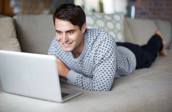 Podekscytowany ściąganiem jego ulubionego serialu. Przycięte ujęcie młodego człowieka używającego laptopa na kanapie. — Zdjęcie stockowe
