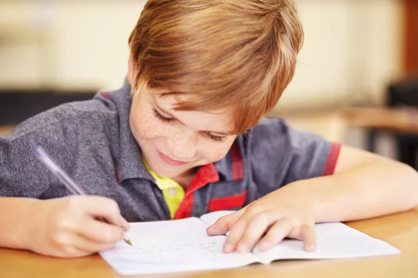 Ik doe graag zijn huiswerk. Een schattig jongetje doet zijn huiswerk in de klas. — Stockfoto