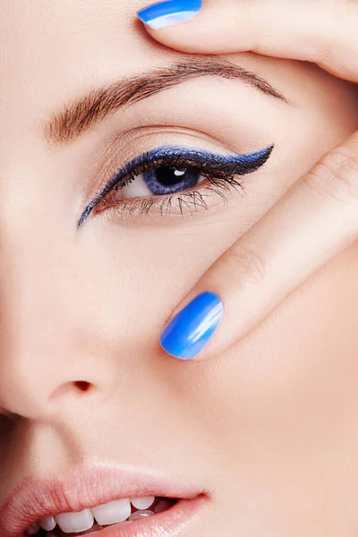 Blau bringt die Augen hervor. Nahaufnahme eines blauen Auges mit blauem Eyeliner mit zwei Fingern mit blauem Nagellack. — Stockfoto