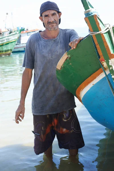 Ser pescador pode ser difícil. Retrato de um pescador em pé na água rasa ao lado de seu barco. — Fotografia de Stock