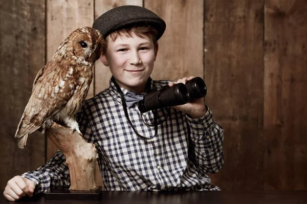 Az ornitológia nagyon szórakoztató. Fiatal fiú retro ruhában távcsövet visel egy bagoly mellett.. — Stock Fotó