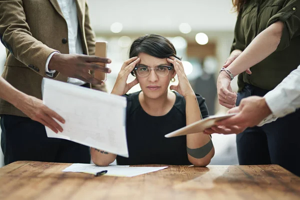 ¿Alguien tiene una pastilla para el dolor de cabeza? Retrato recortado de una joven empresaria que se siente abrumada por sus colegas en la oficina. — Foto de Stock