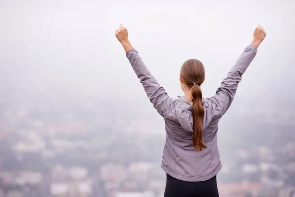 Mi sento in cima al mondo al mattino. Retrovisore di una donna che si allena all'aperto con le braccia tese. — Foto Stock