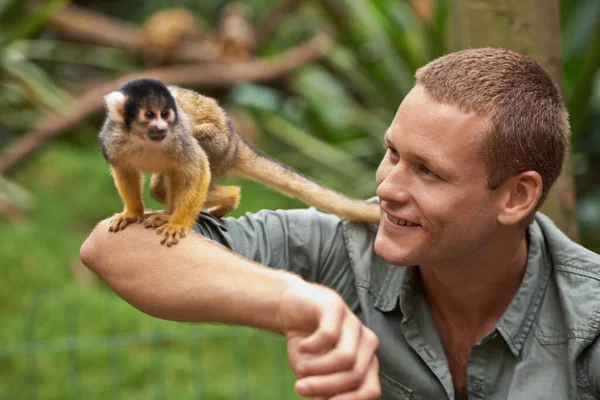 ターザンは友人と過ごすのが好きだった。野生動物公園で小さな猿と交流している若い男のショット. — ストック写真