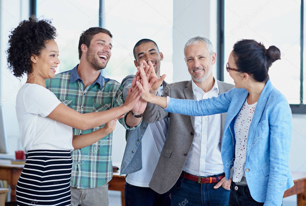 Lets get this done team. Shot of a group of happy coworkers high-fiving while standing in an office.