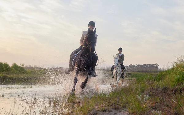 Es wird keine Stunde verschwendet, die im Sattel verbracht wird. Aufnahme von zwei jungen Frauen, die draußen auf einem Feld auf ihren Pferden reiten. — Stockfoto