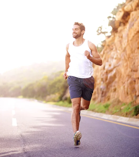 De weg van fitness bewandelen. Full length shot van een knappe jongeman rennend op een weg. — Stockfoto