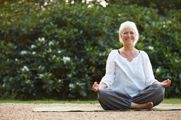 Hon gör mindfulnessövningar utomhus. Porträtt av en attraktiv mogen kvinna som sitter i lotusställning utomhus. — Stockfoto