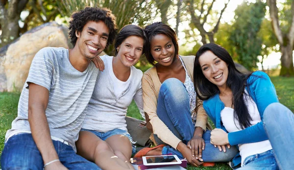 Vysoká rozmanitost. Snímek z různorodé skupiny vysokoškolských studentů sedících venku pomocí digitálního tabletu. — Stock fotografie
