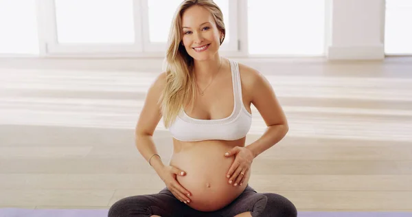 Gezond blijven voor de baby. Gesneden portret van een aantrekkelijke jonge zwangere vrouw wrijven haar baby hobbel terwijl zitten op een yoga mat. — Stockfoto