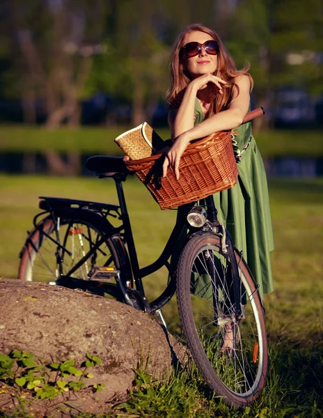 Admirando la tranquilidad de la naturaleza. Foto de una hermosa joven que se relaja en el parque junto a su bicicleta a la antigua. — Foto de Stock