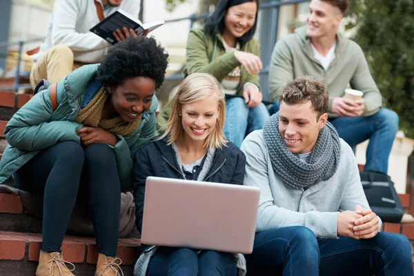 Estamos ansiosos para aprender. Tiro de um grupo de estudantes universitários sorridentes olhando para algo em um laptop. — Fotografia de Stock