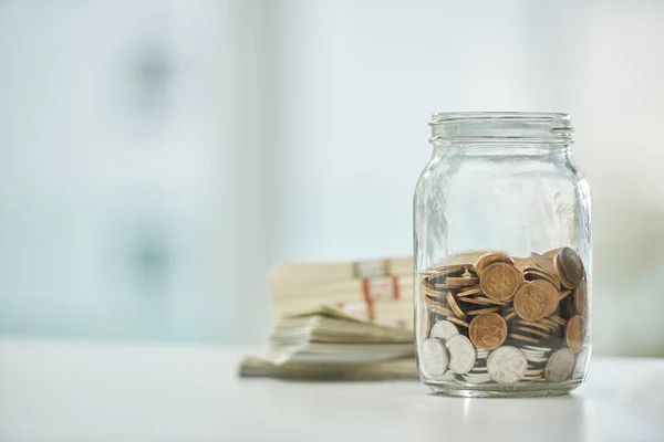 Cada centavo ajuda. Tiro de comprimento cheio de um jarro de moedas e pás de dinheiro em uma mesa em um escritório. — Fotografia de Stock