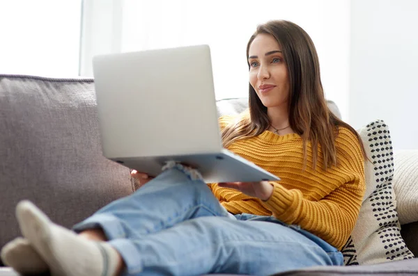 Pasar el día transmitiendo todos los programas que quiere. Foto de una mujer joven usando un ordenador portátil mientras se relaja en un sofá en casa. —  Fotos de Stock