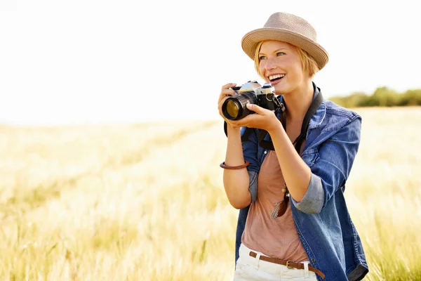 Sie liebt es, die Natur zu fotografieren. Eine attraktive junge Frau hält auf einem Feld eine Kamera in der Hand. — Stockfoto