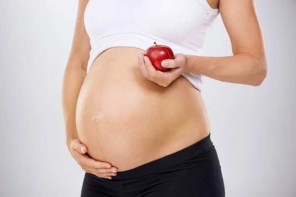 Υγιεινή διατροφή για το μωρό. Καλλιεργημένη εικόνα εγκύου που κρατάει ένα μήλο και αγγίζει το στομάχι της στοργικά. — Φωτογραφία Αρχείου