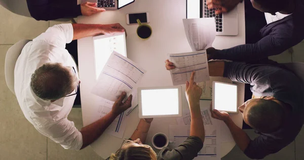 Los turnos tardíos pueden traerte éxito. Foto de alto ángulo de un grupo de empresarios que trabajan juntos alrededor de una mesa en su oficina. —  Fotos de Stock