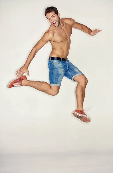 Наповнений витримкою. М'язистий молодий хлопець стрибає в джинсових шортах, перебуваючи на білому тлі . — стокове фото