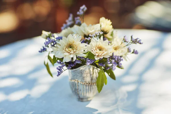 Flores frescas crean el ambiente perfecto para una fiesta de té. Tiro de un jarrón de metal lleno de flores en la mesa en una fiesta de té fuera. — Foto de Stock