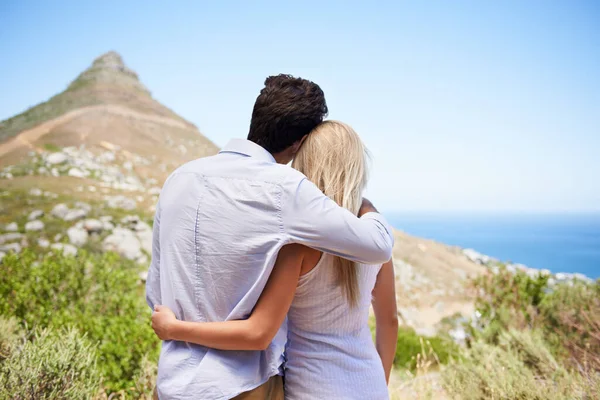Vi har en underbar utsikt. Bakifrån av ett ungt par omfamnar som de har utsikt över berget. — Stockfoto