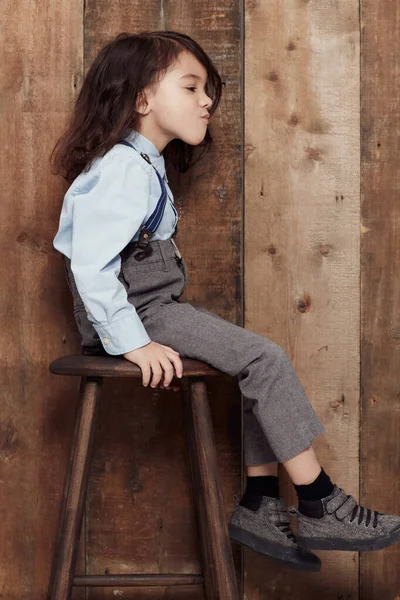 Aku suka gaya lama-sekolah saya. Shot of a cute little boy in old fashioned overalls sitting on a stol. — Stok Foto